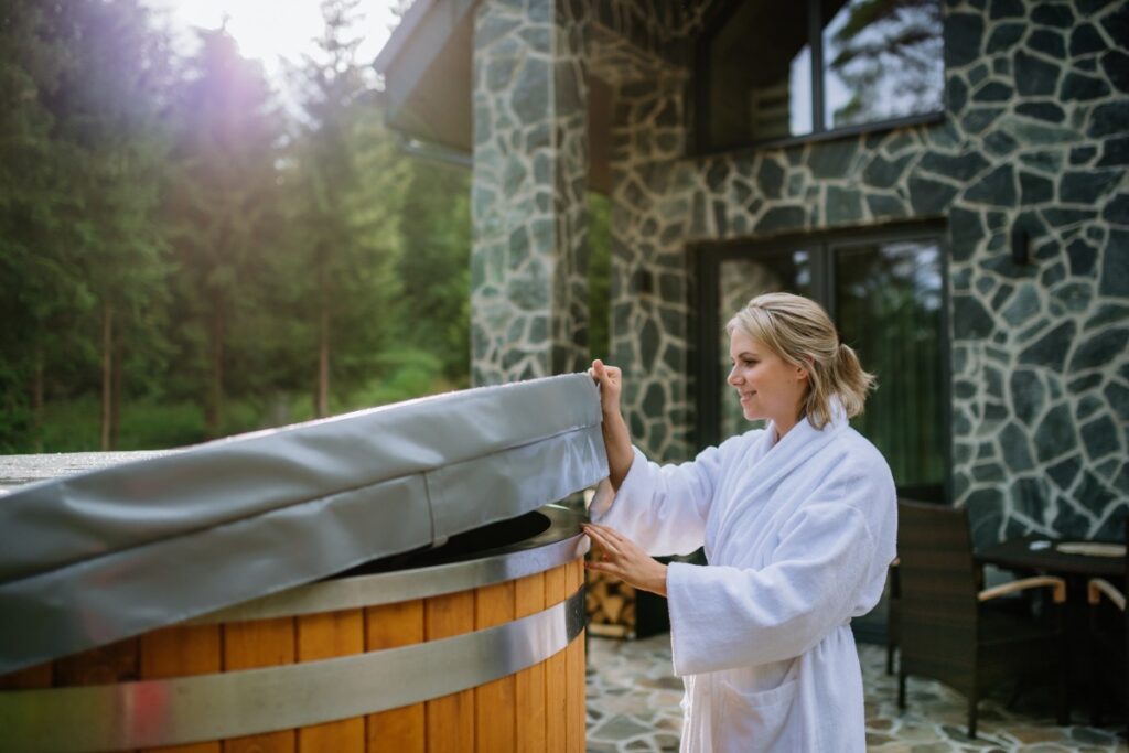 Une jeune femme en peignoir ouvrant le couvercle du spa